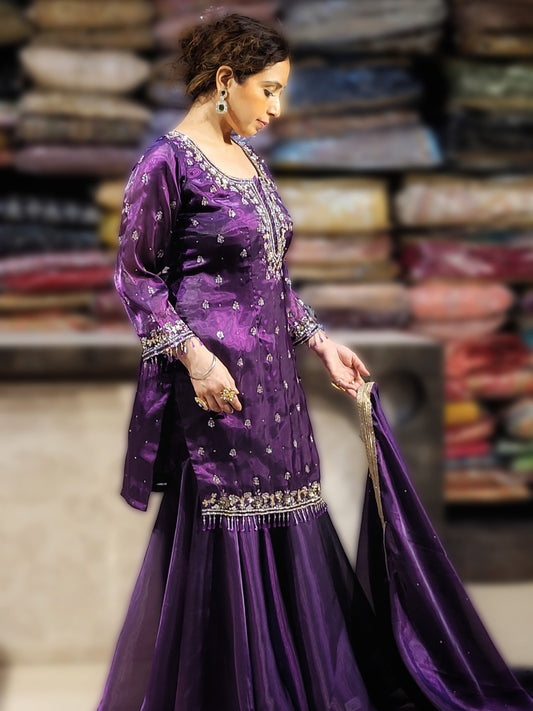Embrace opulence in this mesmerizing purple sharara suit, crafted from the luxurious texture of Jimmy Choo fabric. Shimmer and shine with every step, adorned by intricate zarkan, sequins, and beadwork that dance across the silhouette.