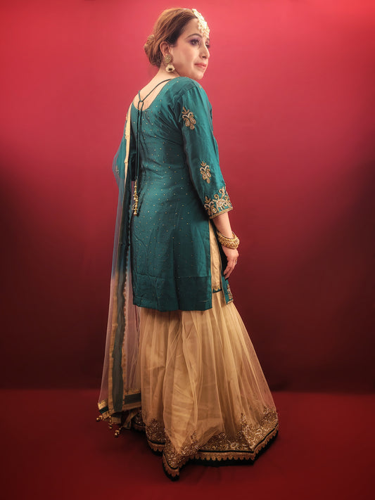 Immerse yourself in opulence with this captivating Rama green silk kameez and golden net gharara set. The luxurious silk kameez drapes beautifully, offering a touch of regal elegance. Intricate zarkan work adorns the kameez, adding a touch of shimmering gold that catches the light with every move.