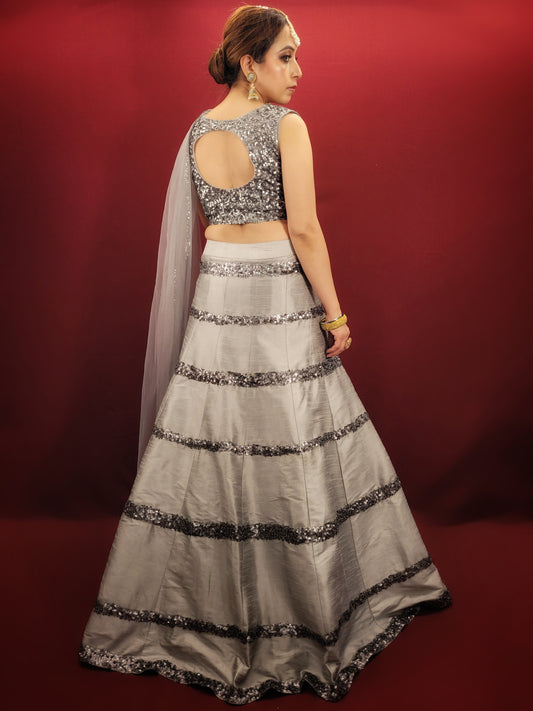 Expertly crafted with silver grey silk, this Lehenga features intricate cutdana beadwork and comes with a matching dupatta. Perfect for any party, it's sure to make you stand out with its elegant design. Elevate your style with this luxurious and timeless piece.