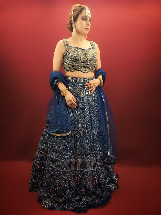 Embrace breathtaking opulence with this exquisite Storm Blue Net Lehenga Choli Set. Crafted from delicate net fabric, this ensemble drapes beautifully, creating a silhouette that is both ethereal and undeniably glamorous. Prepare to be swept away by the unparalleled embellishments that adorn this masterpiece.