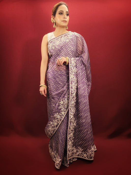 Wrap yourself in the vibrant hues of a purple & white leheriya saree crafted from sheer organza and embellished with beautiful Pitta work, a statement piece for any occasion.