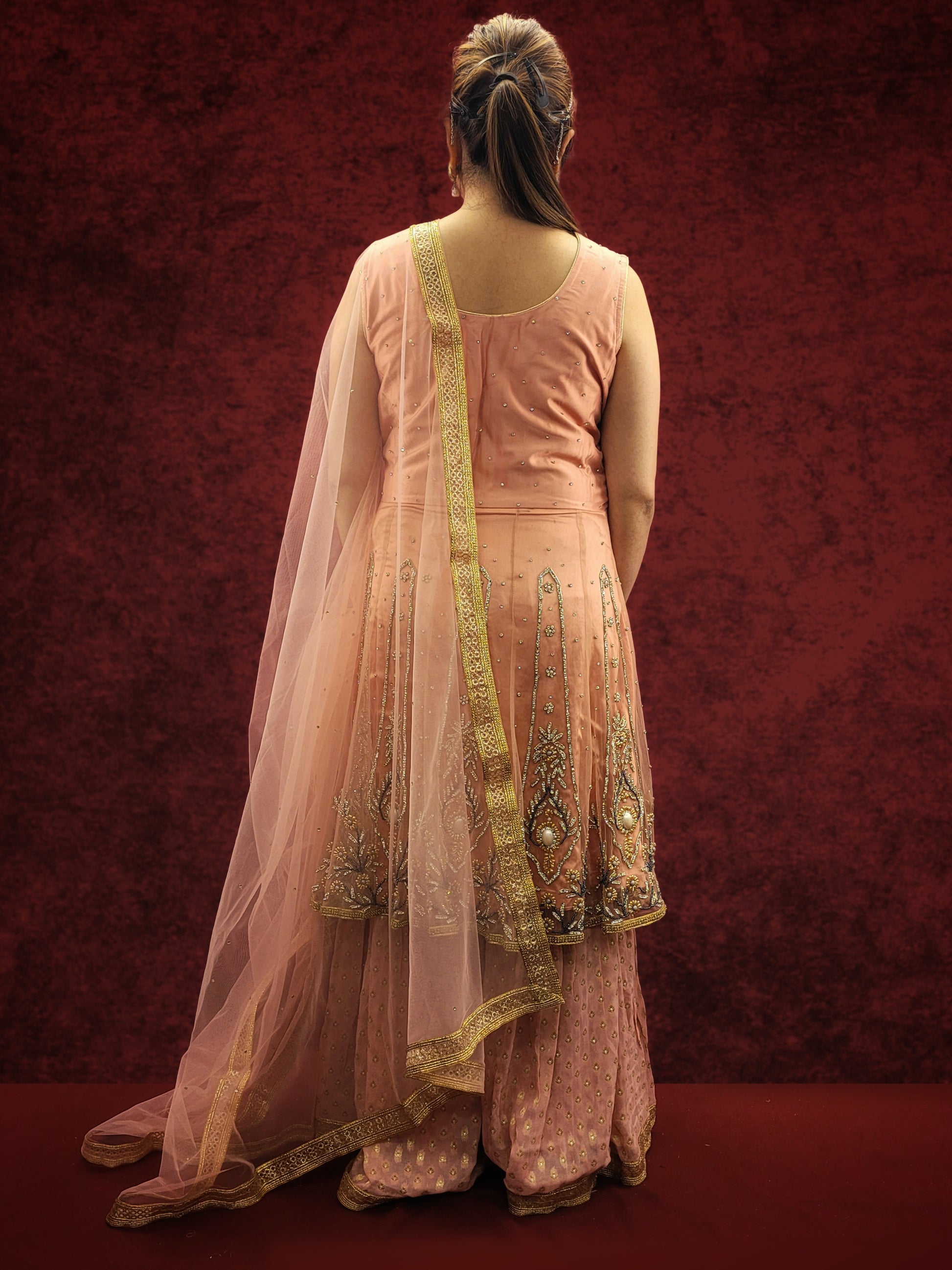 A pink indo-western ensemble featuring a net peplum top adorned with zarkan and beads, paired with a luxurious khaddi banarsi gharara, exudes a blend of contemporary flair and classic elegance.