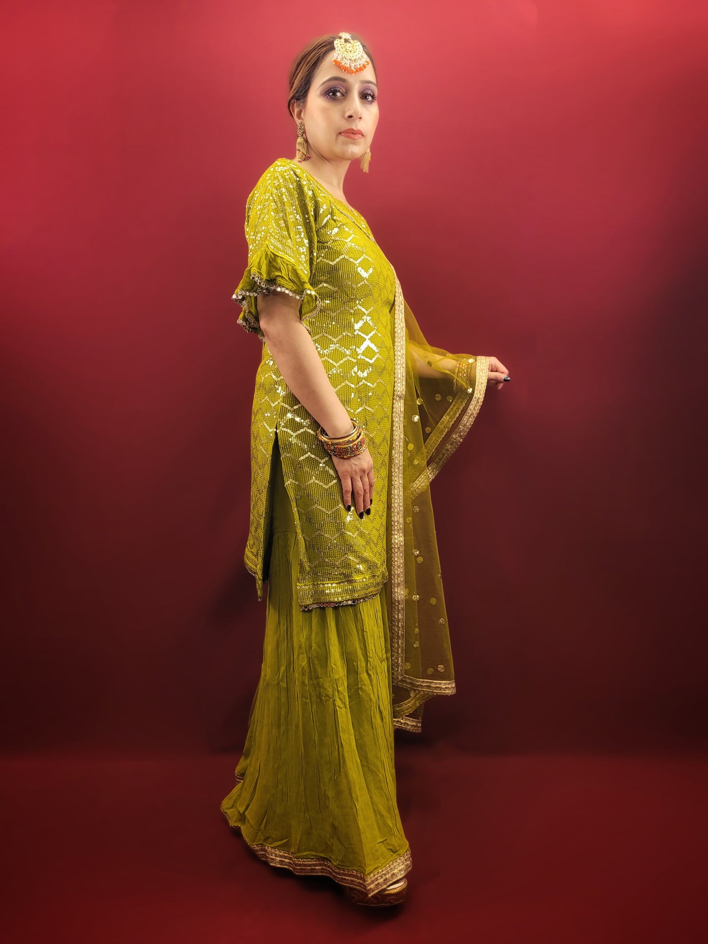 Embrace elegance with a mehendi green sharara set, featuring a dazzling sequins work and a beads & zari embellished neckline, crafted from luxurious chinnon fabric for a quintessential Indian ethnic wear ensemble.
