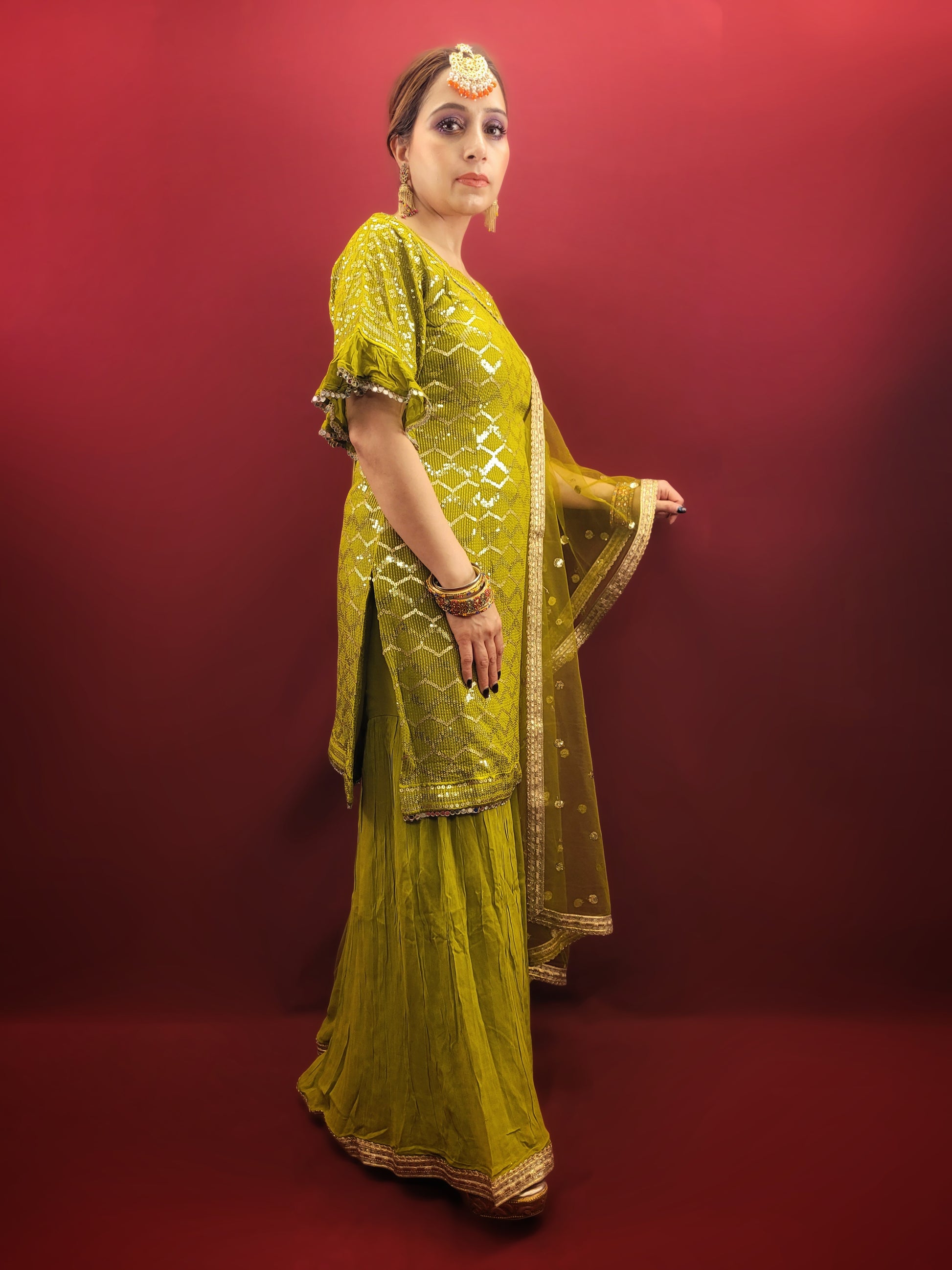 Embrace elegance with a mehendi green sharara set, featuring a dazzling sequins work and a beads & zari embellished neckline, crafted from luxurious chinnon fabric for a quintessential Indian ethnic wear ensemble.