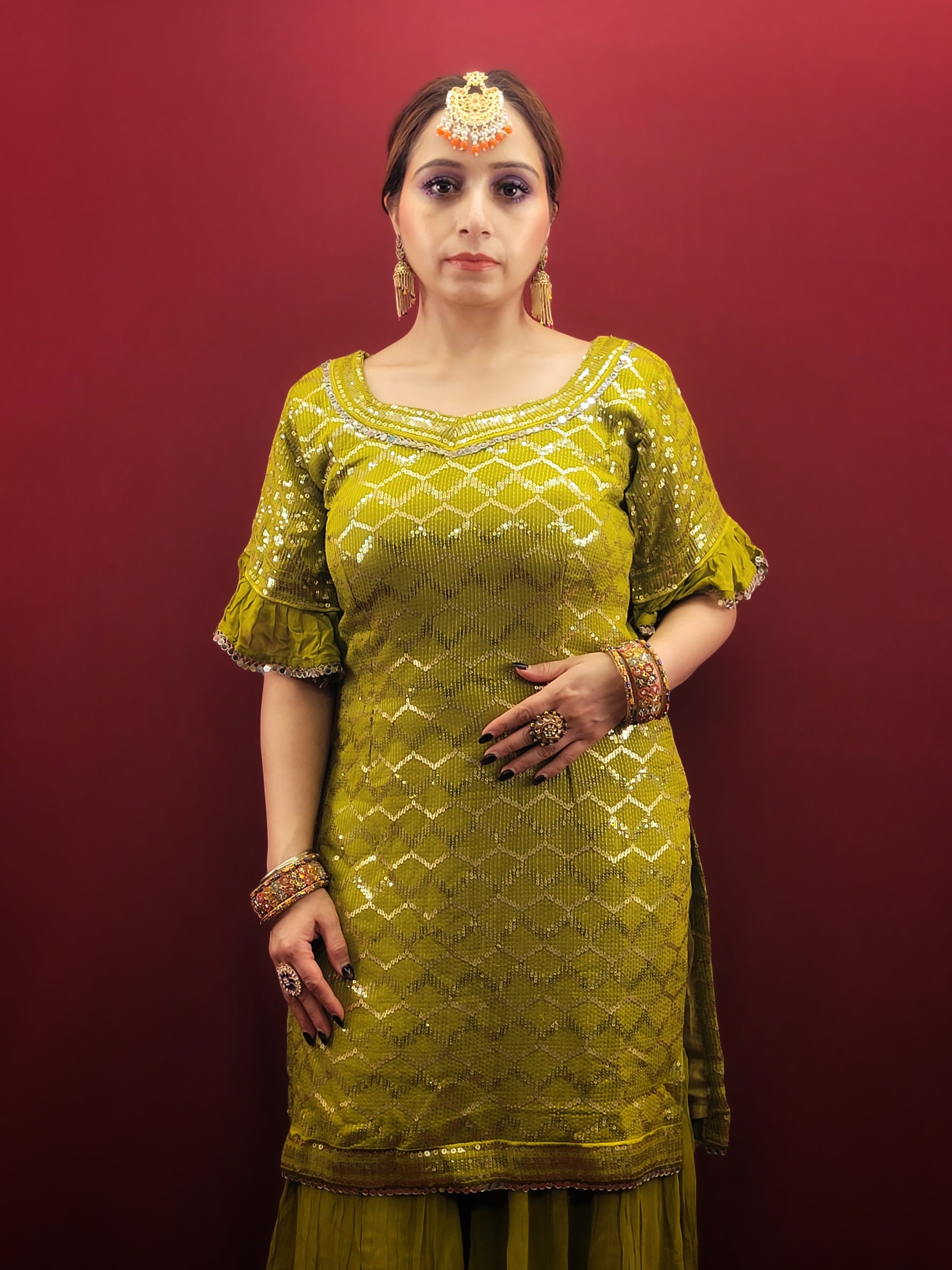 Embrace elegance with a mehendi green sharara set, featuring a dazzling sequins work and a beads & zari embellished neckline, crafted from luxurious chinnon fabric for a quintessential Indian ethnic wear ensemble.