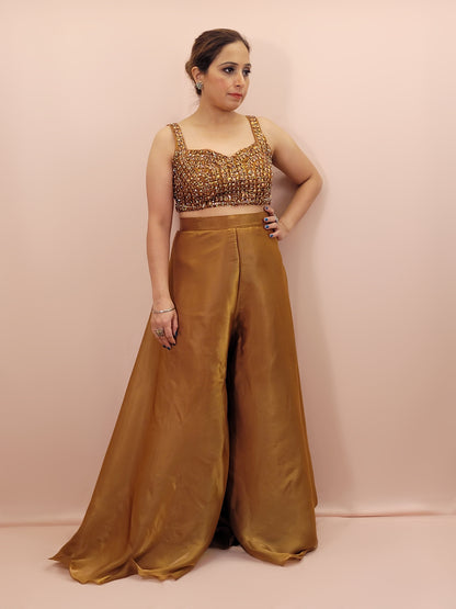 Elevate your festive wardrobe with our Golden Brown Shimmer Pallazo Top Indowestern Fusion Set - a perfect blend of tradition and modernity. This stunning ensemble features a sleeveless cropped blouse adorned with exquisite beadwork and sparkling sequins that catch the light beautifully. Paired with a high-waisted, flowing Pallazo in luxurious grey Jimmy Choo fabric, this outfit promises an elegant silhouette and timeless grace.