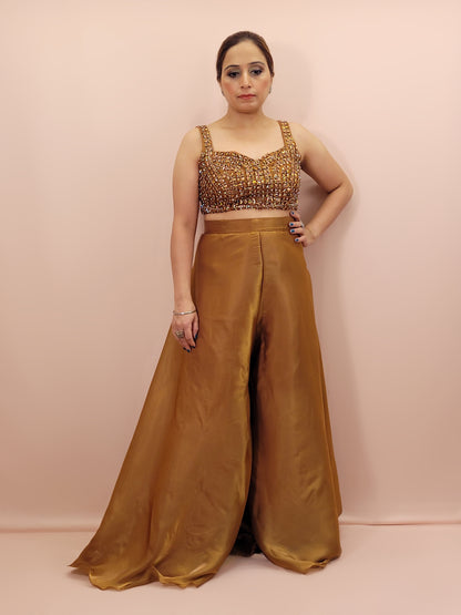 Elevate your festive wardrobe with our Golden Brown Shimmer Pallazo Top Indowestern Fusion Set - a perfect blend of tradition and modernity. This stunning ensemble features a sleeveless cropped blouse adorned with exquisite beadwork and sparkling sequins that catch the light beautifully. Paired with a high-waisted, flowing Pallazo in luxurious grey Jimmy Choo fabric, this outfit promises an elegant silhouette and timeless grace.