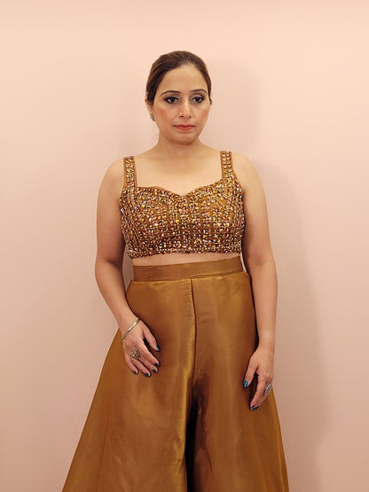 Elevate your festive wardrobe with our Golden Brown Shimmer Pallazo Top Indowestern Fusion Set - a perfect blend of tradition and modernity. This stunning ensemble features a sleeveless cropped blouse adorned with exquisite beadwork and sparkling sequins that catch the light beautifully. Paired with a high-waisted, flowing Pallazo in luxurious grey Jimmy Choo fabric, this outfit promises an elegant silhouette and timeless grace.