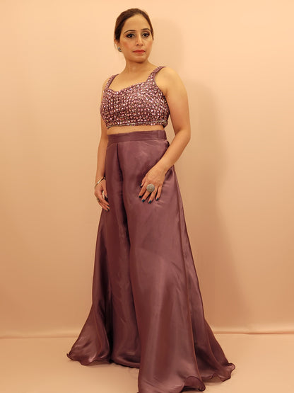 levate your festive wardrobe with our Mauve Shimmer Pallazo Top Indowestern Fusion Set - a perfect blend of tradition and modernity. This stunning ensemble features a sleeveless cropped blouse adorned with exquisite beadwork and sparkling sequins that catch the light beautifully. Paired with a high-waisted, flowing Pallazo in luxurious grey Jimmy Choo fabric, this outfit promises an elegant silhouette and timeless grace.
