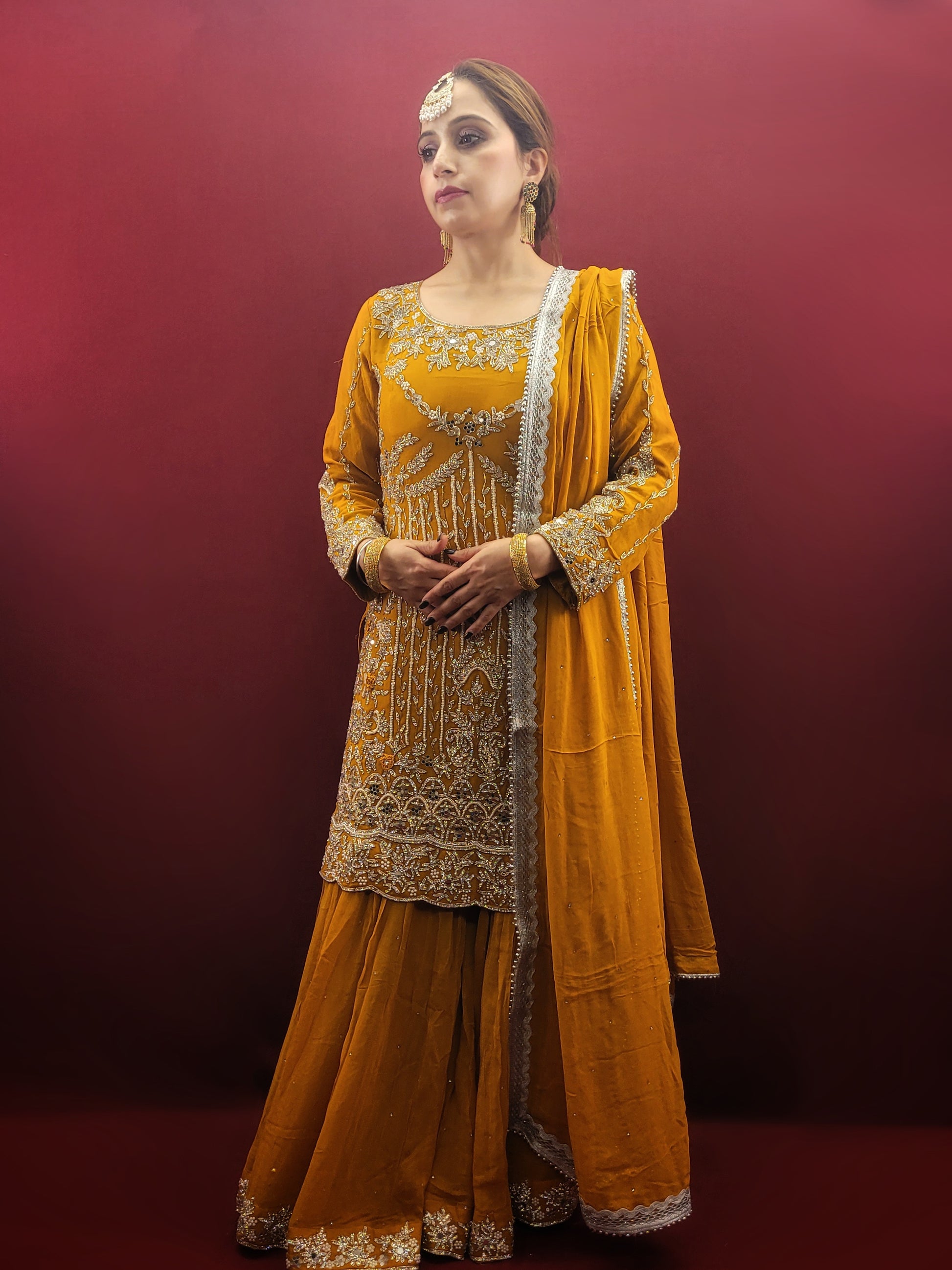 A mustard yellow georgette kameez gharara set, embellished with sparkling zarkan and zardozi work, radiates traditional charm, perfect for bridal and wedding attire.
