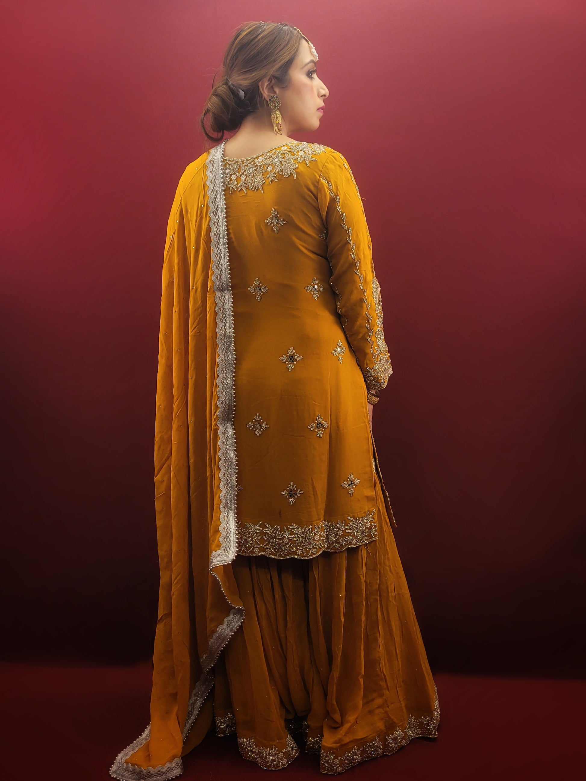 A mustard yellow georgette kameez gharara set, embellished with sparkling zarkan and zardozi work, radiates traditional charm, perfect for bridal and wedding attire.