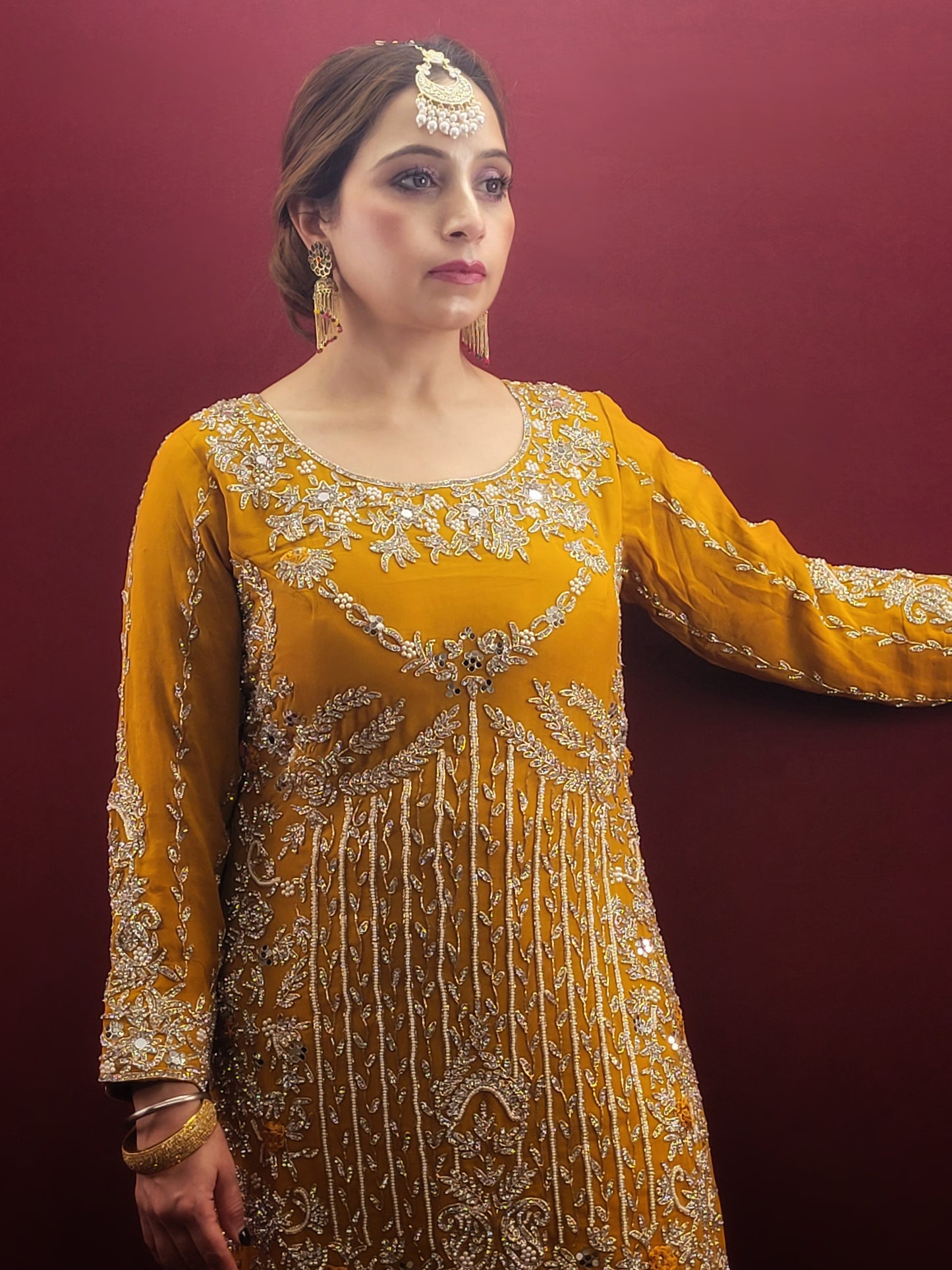 A mustard yellow georgette kameez gharara set, embellished with sparkling zarkan and zardozi work, radiates traditional charm, perfect for bridal and wedding attire.