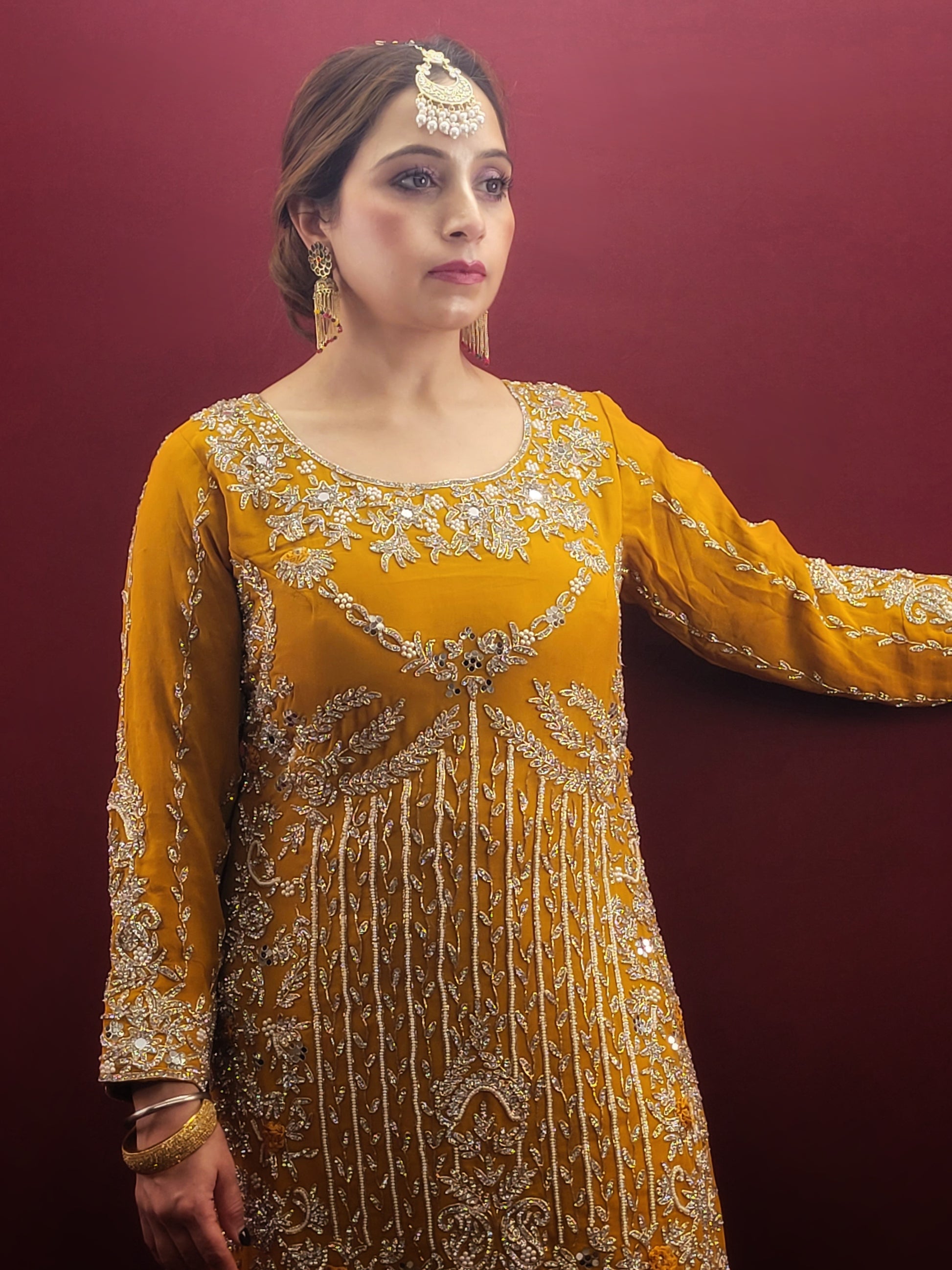 A mustard yellow georgette kameez gharara set, embellished with sparkling zarkan and zardozi work, radiates traditional charm, perfect for bridal and wedding attire.