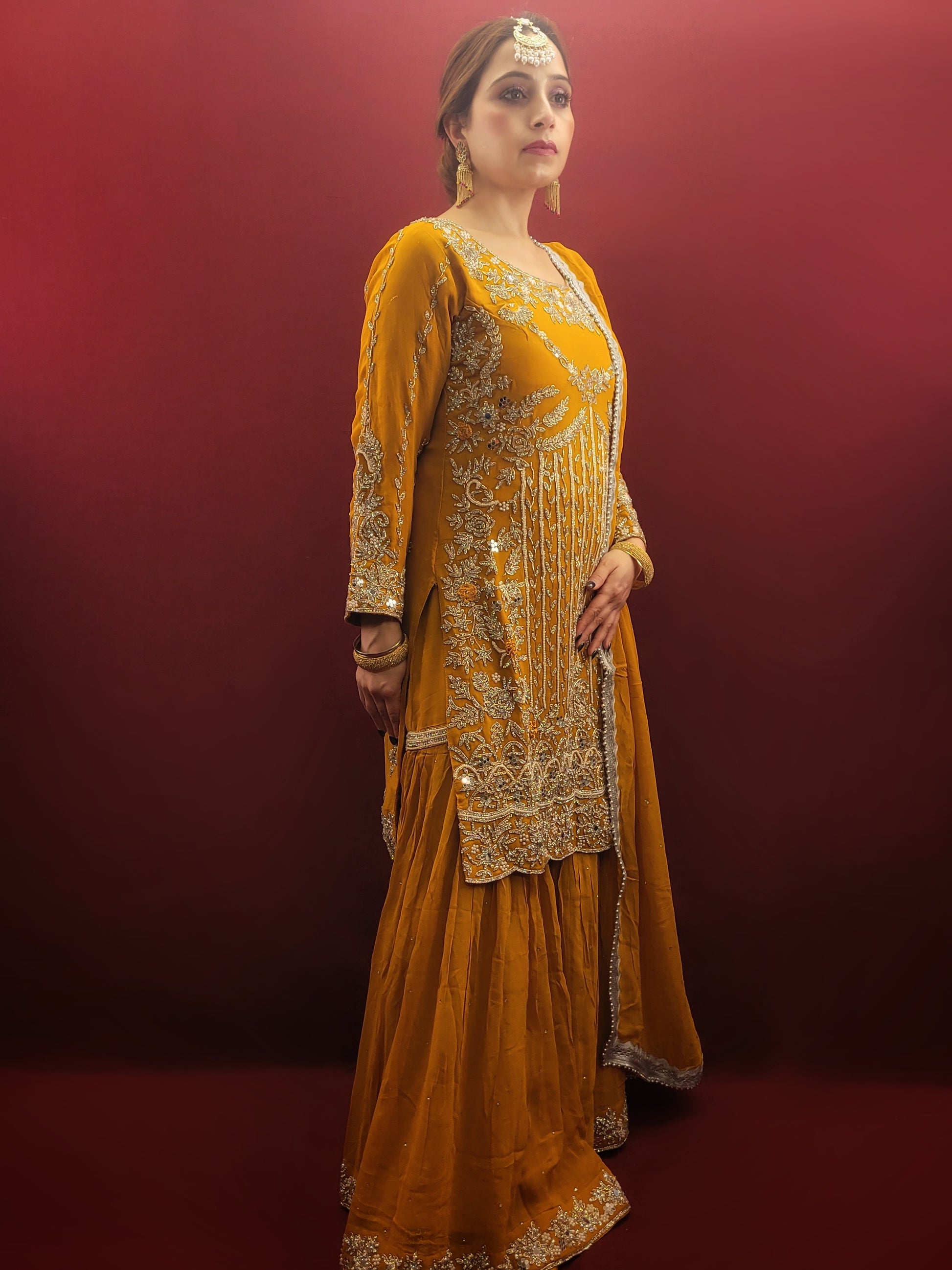 A mustard yellow georgette kameez gharara set, embellished with sparkling zarkan and zardozi work, radiates traditional charm, perfect for bridal and wedding attire.