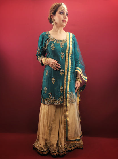 Immerse yourself in opulence with this captivating Rama green silk kameez and golden net gharara set. The luxurious silk kameez drapes beautifully, offering a touch of regal elegance. Intricate zarkan work adorns the kameez, adding a touch of shimmering gold that catches the light with every move.