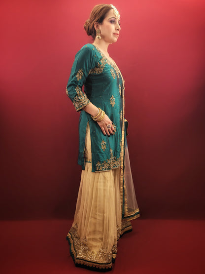Immerse yourself in opulence with this captivating Rama green silk kameez and golden net gharara set. The luxurious silk kameez drapes beautifully, offering a touch of regal elegance. Intricate zarkan work adorns the kameez, adding a touch of shimmering gold that catches the light with every move.