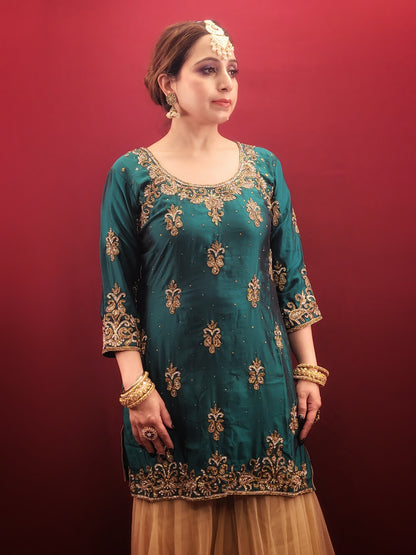 Immerse yourself in opulence with this captivating Rama green silk kameez and golden net gharara set. The luxurious silk kameez drapes beautifully, offering a touch of regal elegance. Intricate zarkan work adorns the kameez, adding a touch of shimmering gold that catches the light with every move.