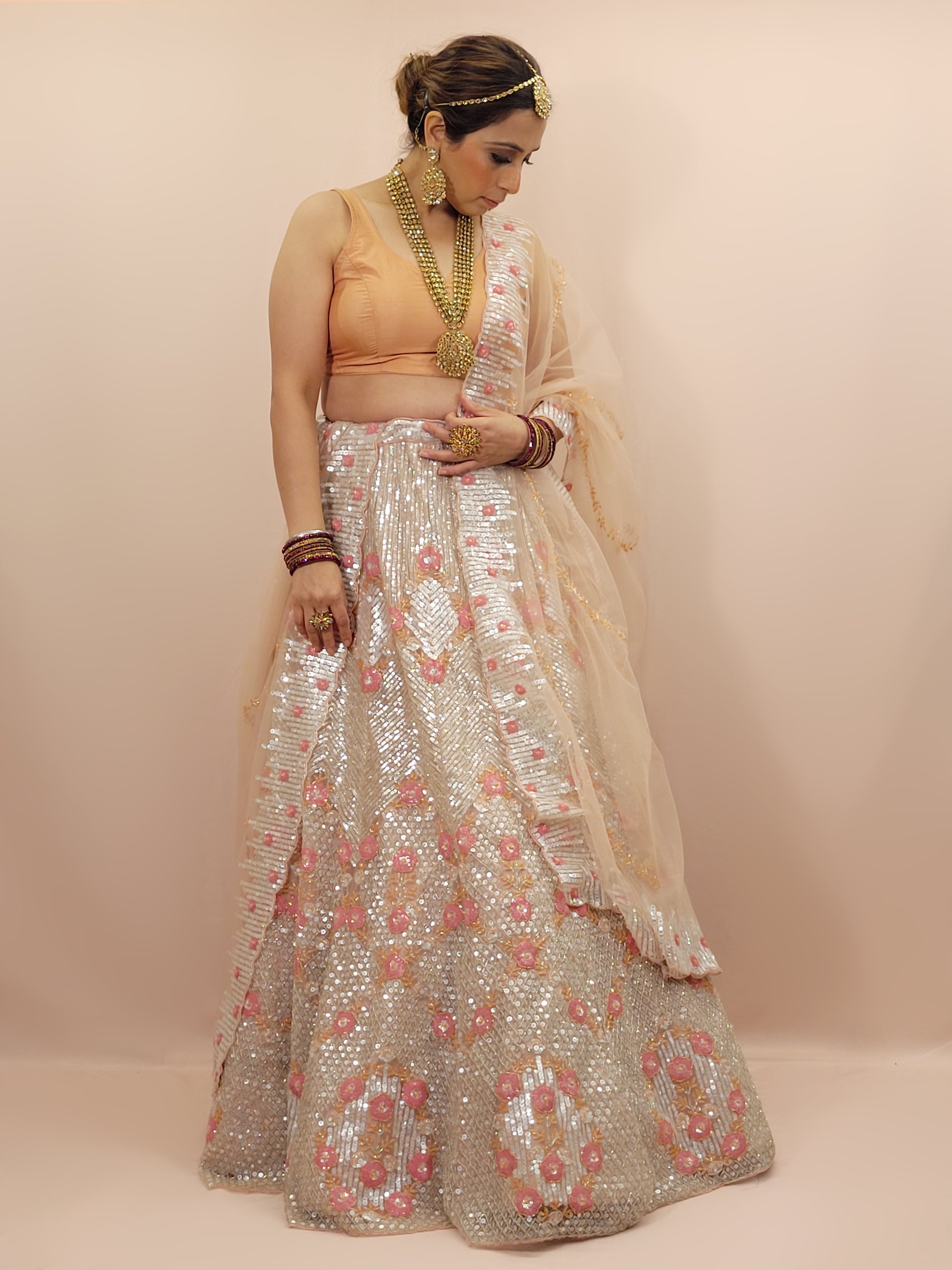 Elevate your ethnic wardrobe with this stunning ivory-colored net unstitched lehenga, a perfect blend of traditional craftsmanship and contemporary elegance. This lehenga is intricately adorned with shimmering water sequins and delicate glass beads work, creating a mesmerizing effect that catches the light with every movement.