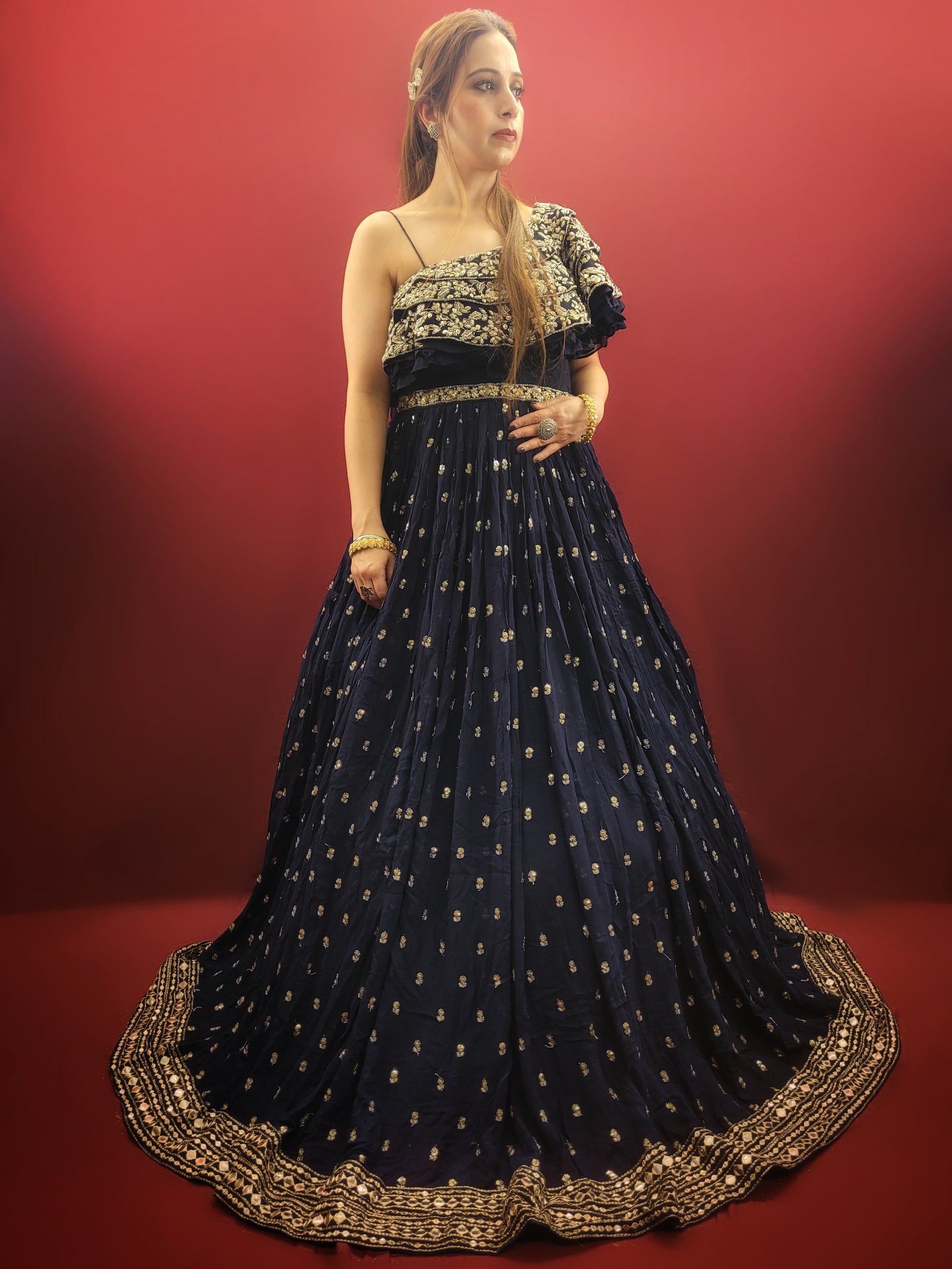 Embrace a captivating silhouette in this stunning navy blue georgette gown. The luxurious fabric drapes elegantly, offering both comfort and a touch of sophistication. The eye-catching one-shoulder design adds a touch of modern allure, while the layered bodice takes center stage with a dazzling display of craftsmanship.