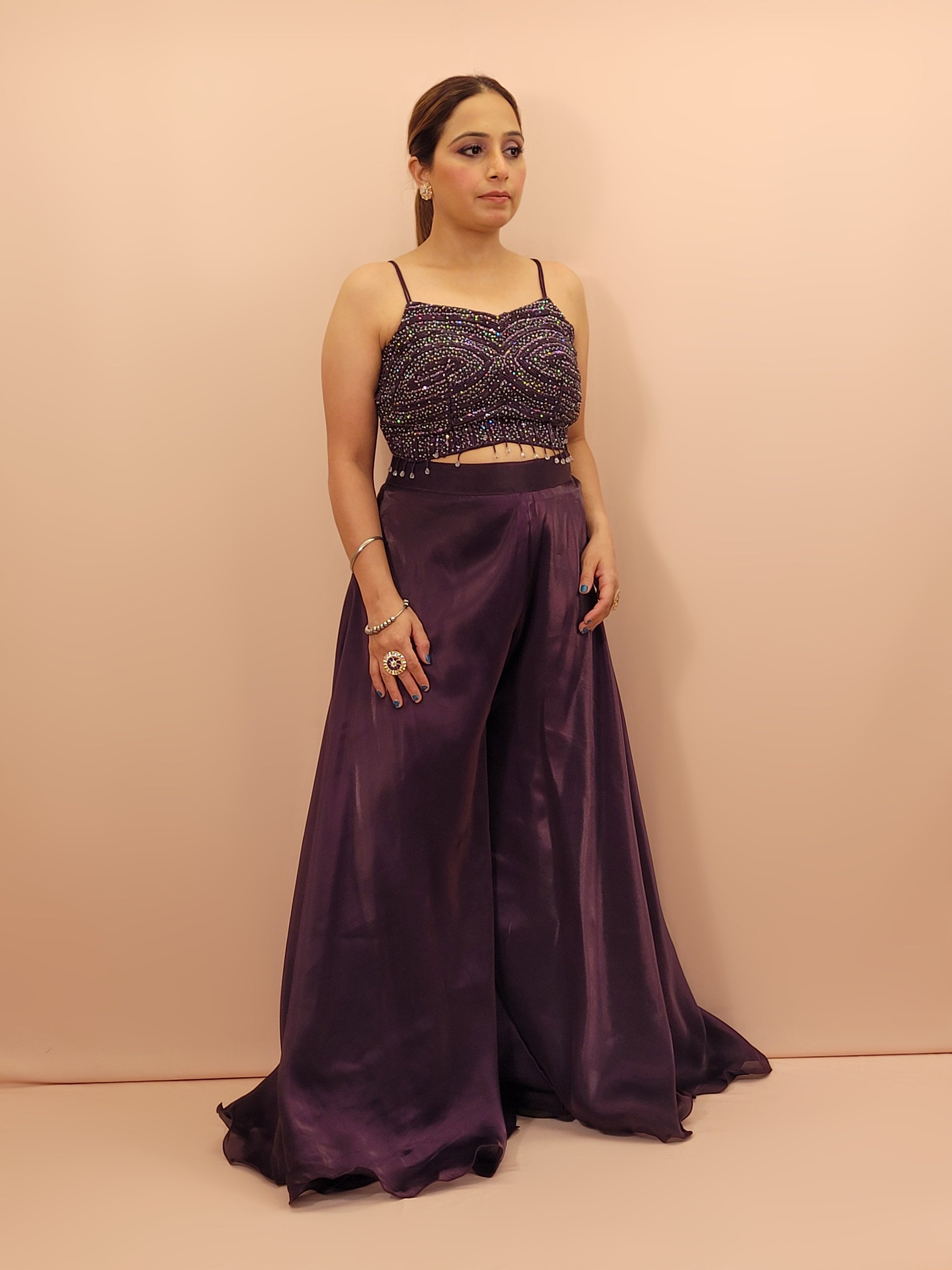 Elevate your festive wardrobe with our Purple Shimmer Pallazo Top Indowestern Fusion Set - a perfect blend of tradition and modernity. This stunning ensemble features a sleeveless cropped blouse adorned with exquisite beadwork and sparkling sequins that catch the light beautifully. Paired with a high-waisted, flowing Pallazo in luxurious Purple Jimmy Choo fabric, this outfit promises an elegant silhouette and timeless grace. Ideal for weddings, celebrations, or any special event
